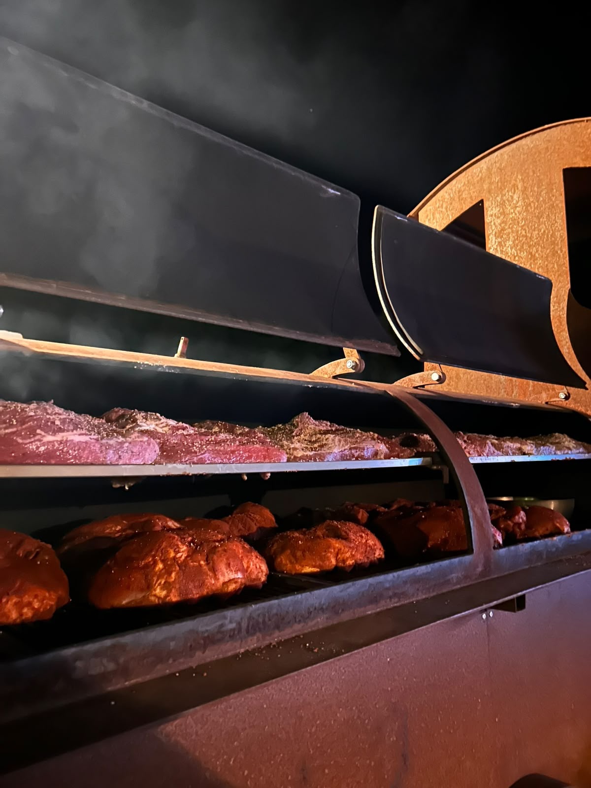 Geöffnete Grilllok mit Fleisch auf zwei Rostebenen im Abendlicht